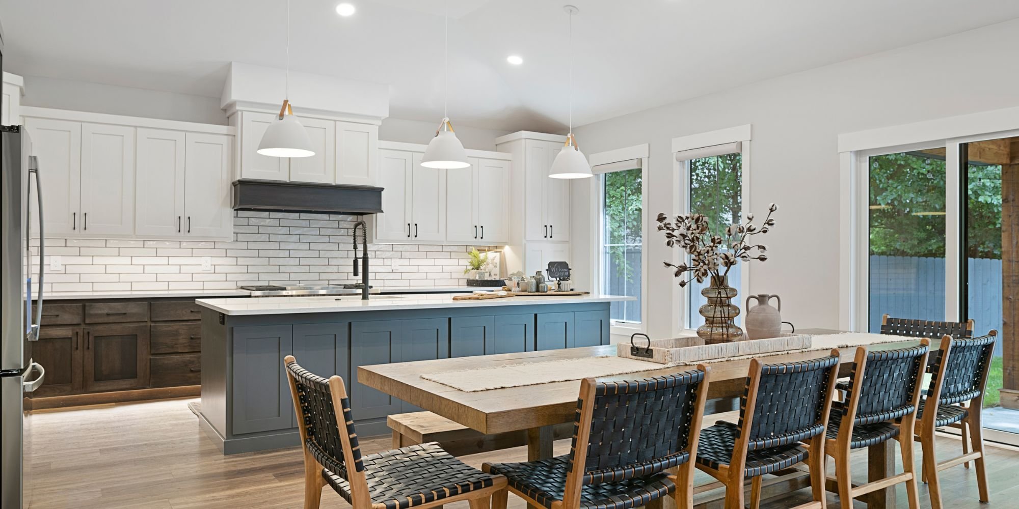 Open-concept kitchen remodel with a blue sink island, large dining table, white upper cabinetry, and wood lower cabinetry by Fox Home Innovations in Manhattan, KS