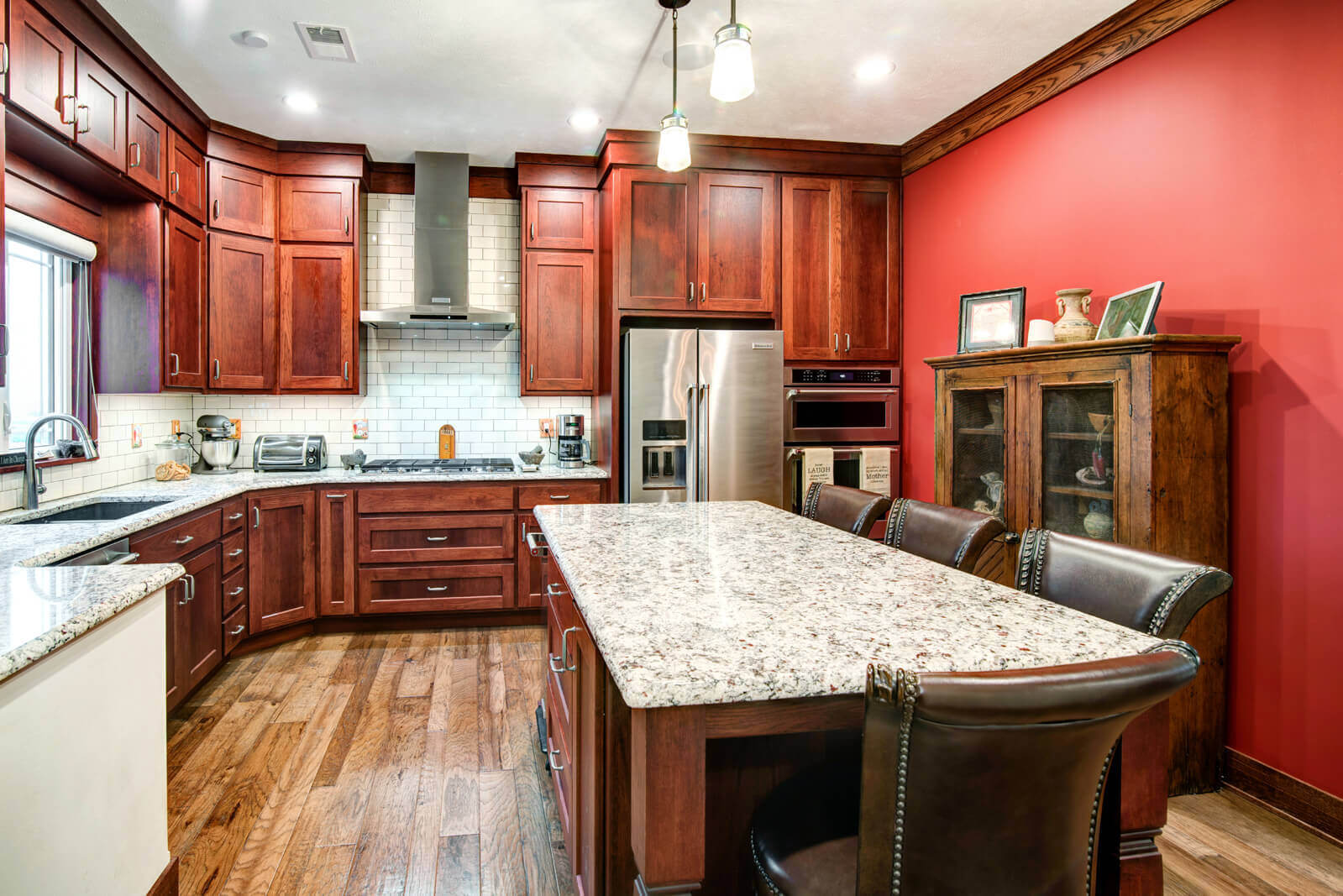 A kitchen remodel in Manhattan, KS featuring red walls, warm natural wood cabinetry, and granite countertops by Fox Home Innovations