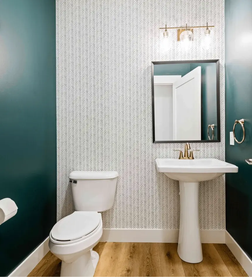 Bathroom with wallpaper accent wall, pedestal sink, and gold finishes.